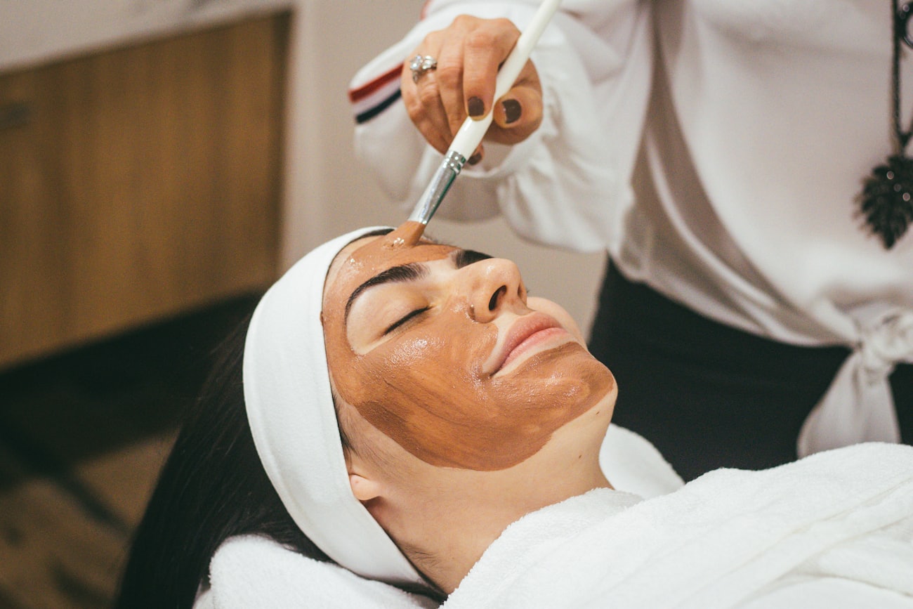 Esteticista aplicando una mascarilla de arcilla con pincel sobre el rostro de una clienta