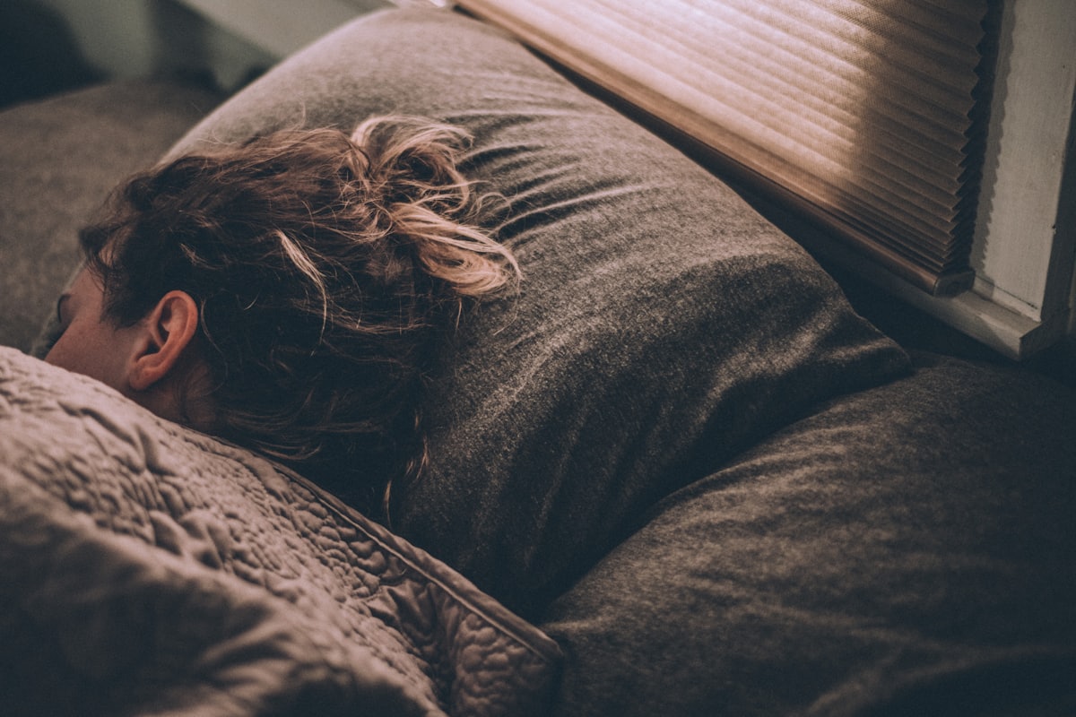 Persona durmiendo de lado en una cama, con luz suave entrando por la persiana