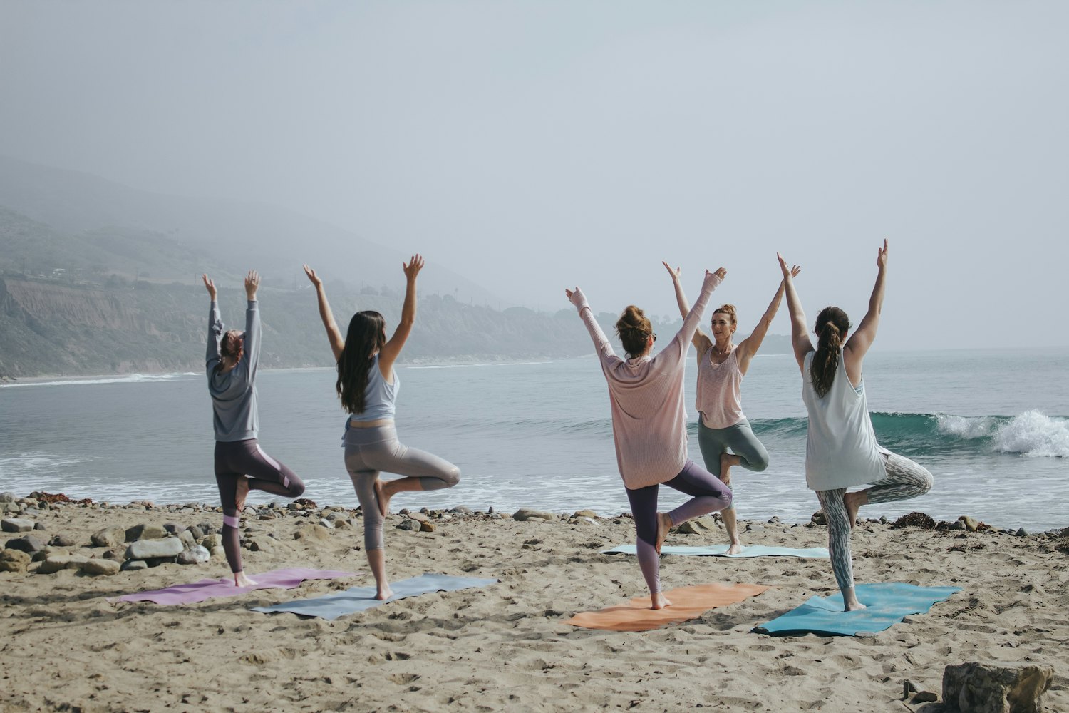 Grupo de personas practicando yoga al amanecer en una playa con bruma